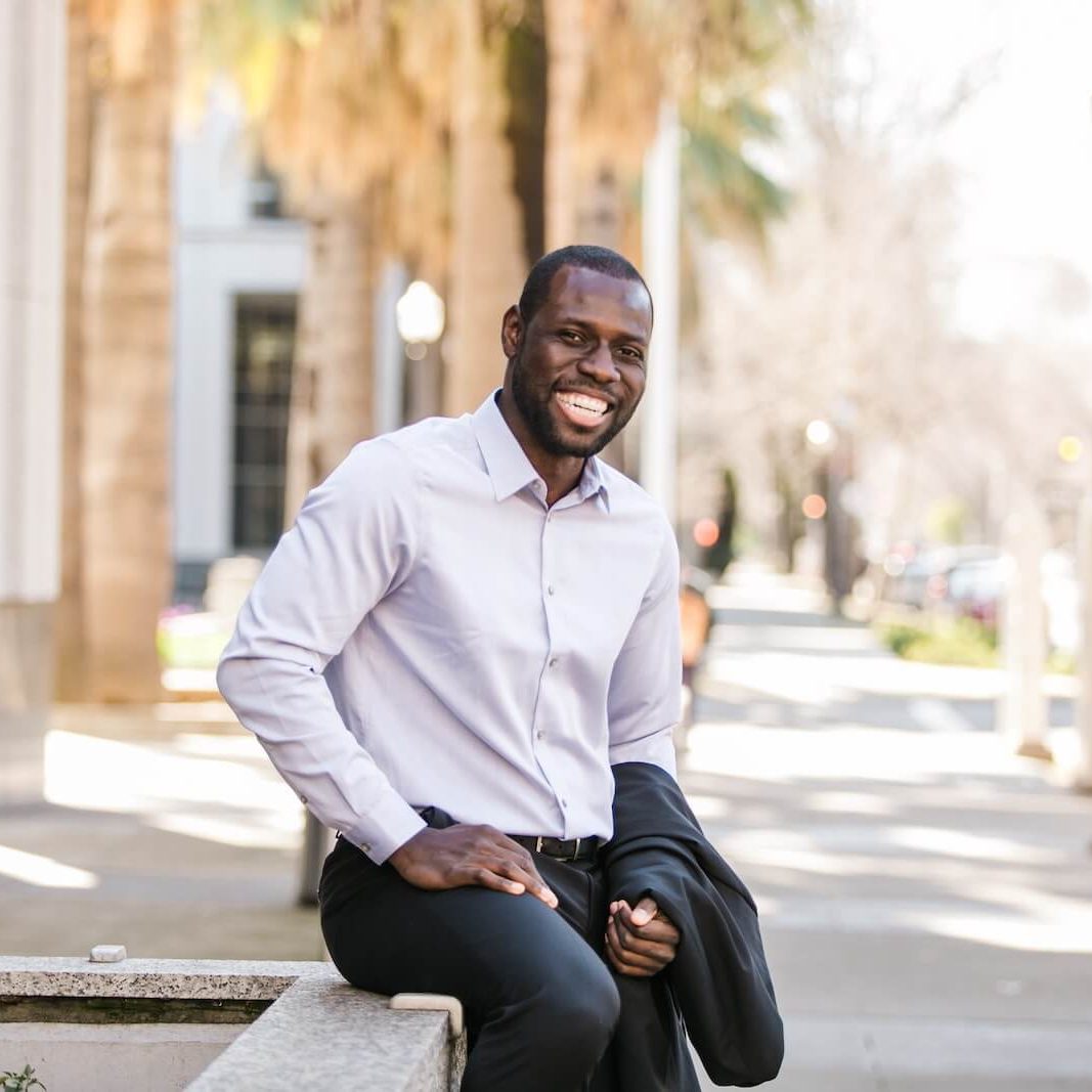 man in white dress shirt and black pants sitting on the sidewalk during daytime